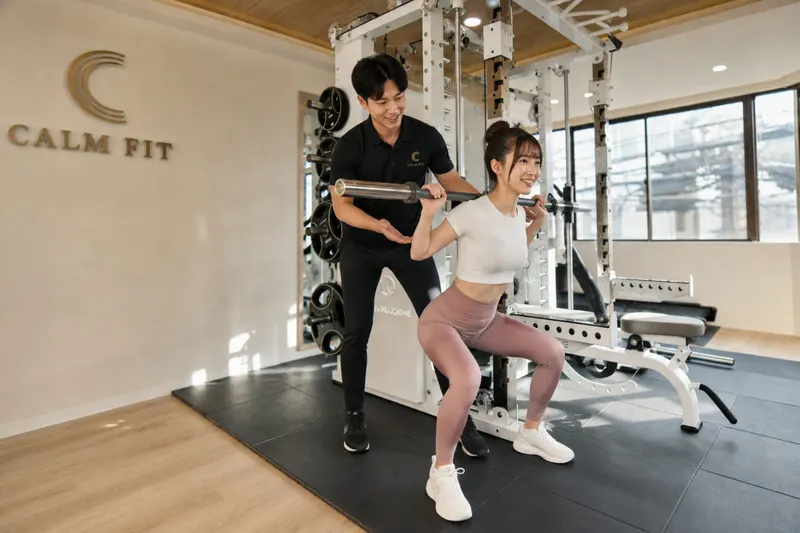 CALM FITの貸切ルームで、トレーナーがバーベルスクワットをマンツーマンでサポート